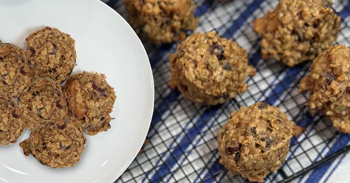 A white plate with six oatmeal cookies sits on a blue checkered cloth next to more cookies on a cooling rack, conveying warmth and homemade appeal.