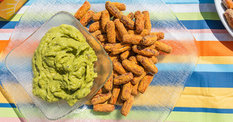Cheddar Jalapeño OMG! Pretzels on a glass plate with a bowl of fresh guacamole on a colorful table