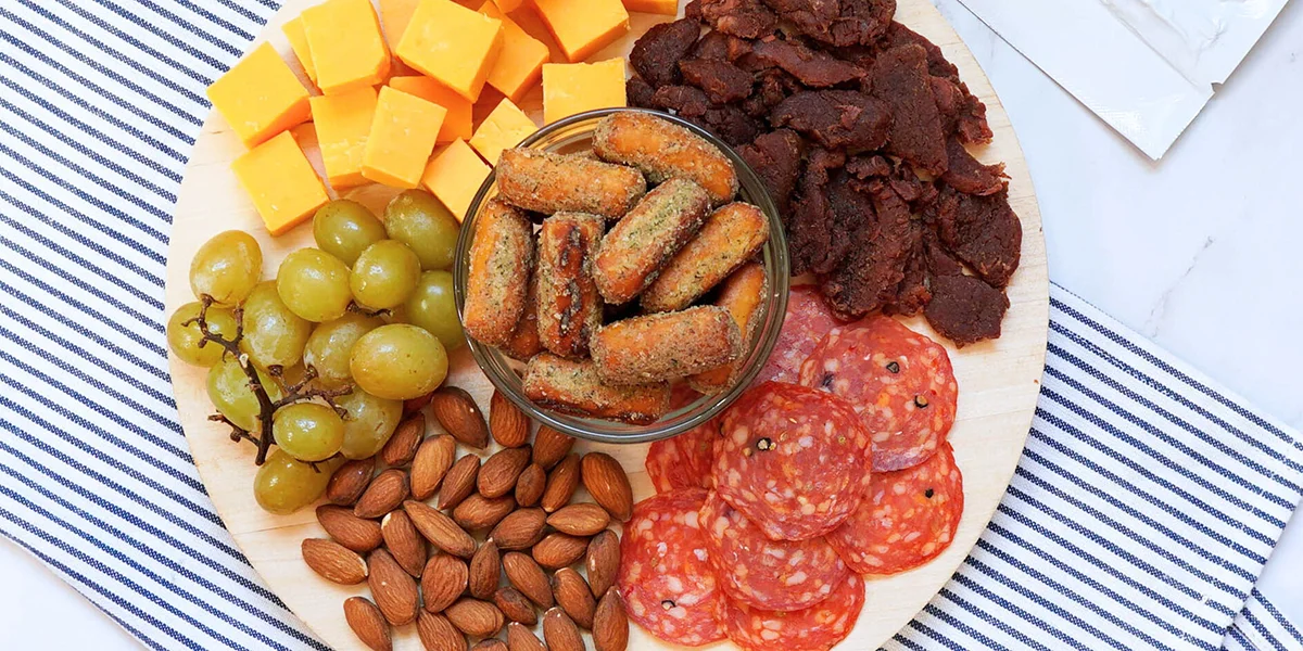 A platter featuring an assortment of cheese, cured meats, nuts, and fresh grapes arranged artfully.