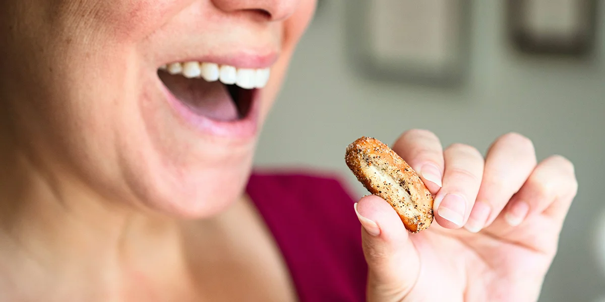 A woman playfully holds a cookie in her mouth, smiling with a lighthearted expression.
