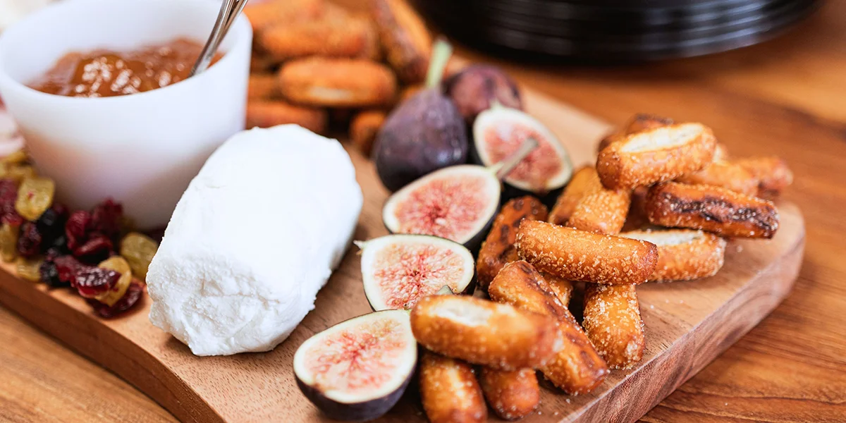 A wooden cutting board displays fresh figs, slices of cheese, and artisanal bread arranged artfully.