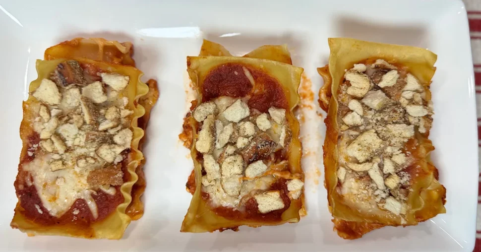 Three lasagna rolls neatly arranged on a white plate, showcasing layers of pasta, cheese, and sauce.