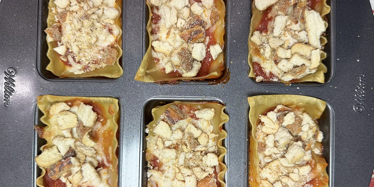 A pan containing six mini lasagnas, each layered with pasta, cheese, and sauce, ready to be served.