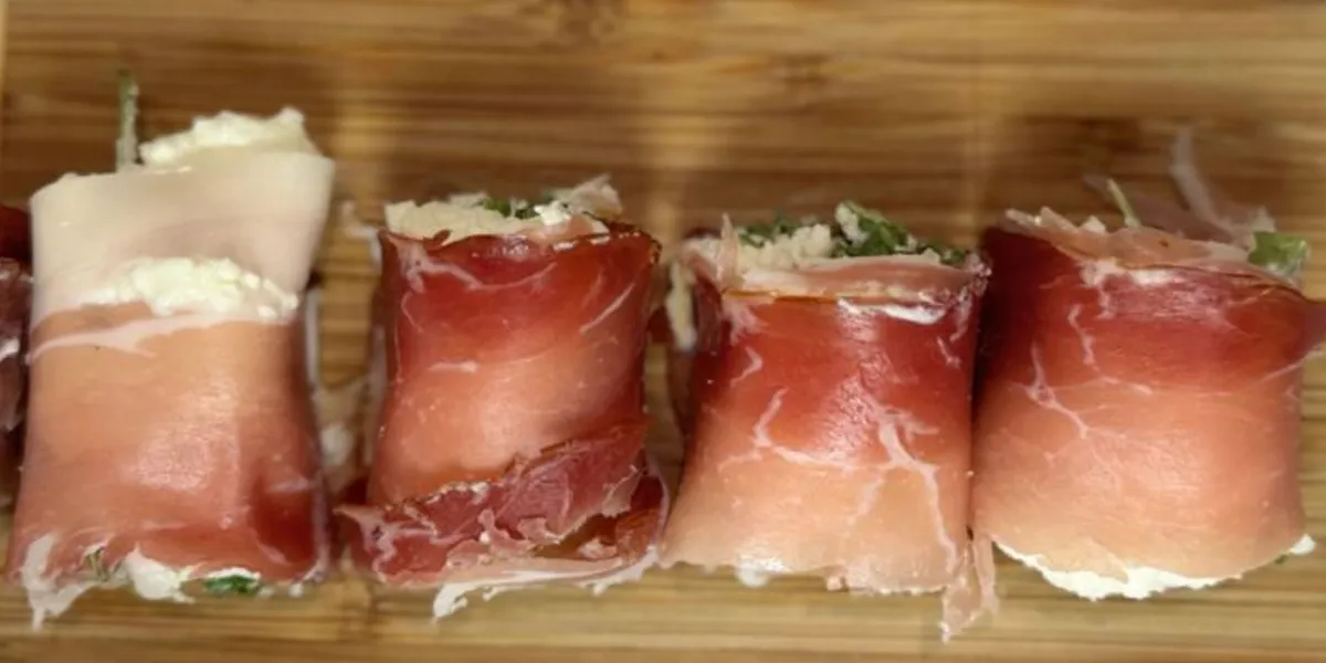 A group of neatly wrapped ham slices arranged on a wooden cutting board, representing Italian sushi preparation.