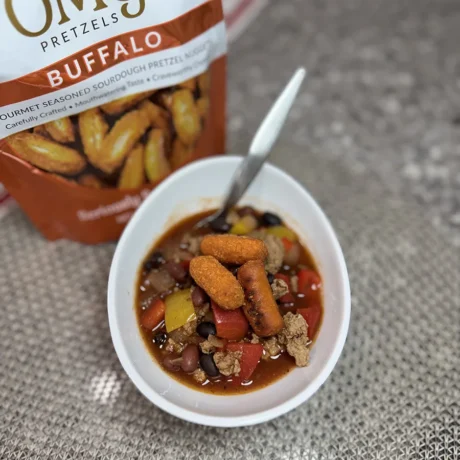 A bowl of buffalo chicken chili soup, featuring shredded chicken, beans, and a spicy orange broth garnished with green onions.