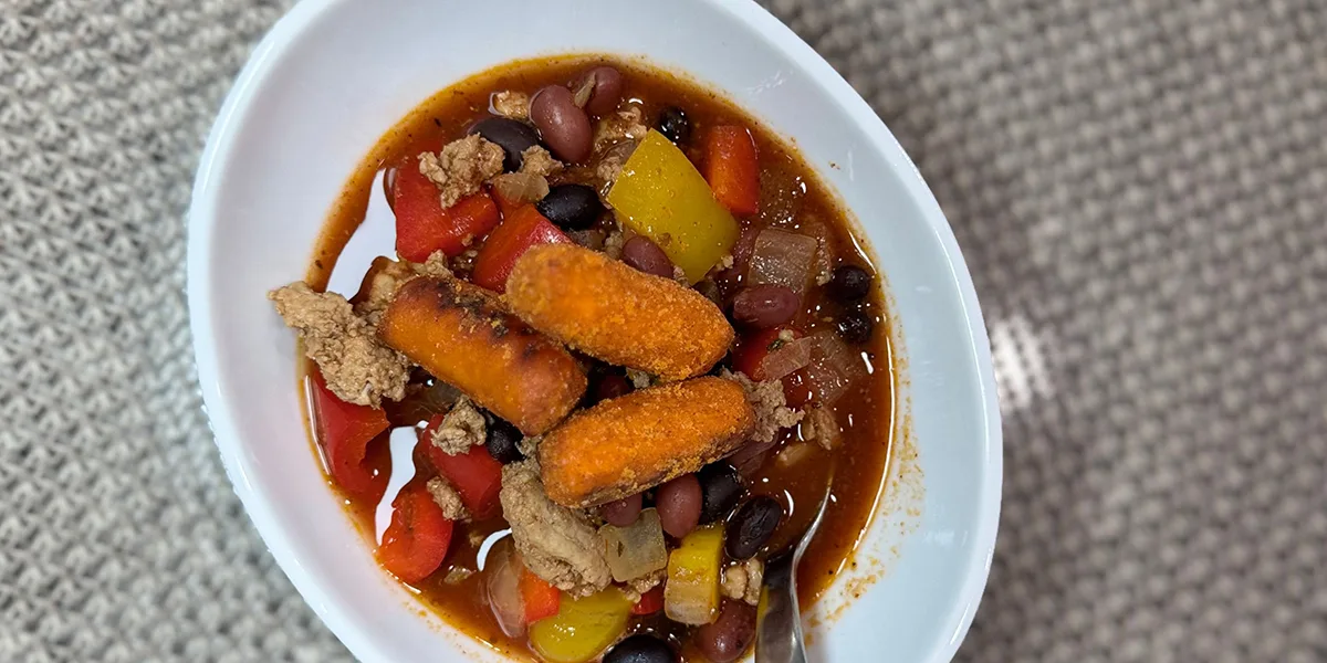 A bowl of hearty chili filled with meat, beans, and colorful vegetables, garnished with a sprinkle of herbs.