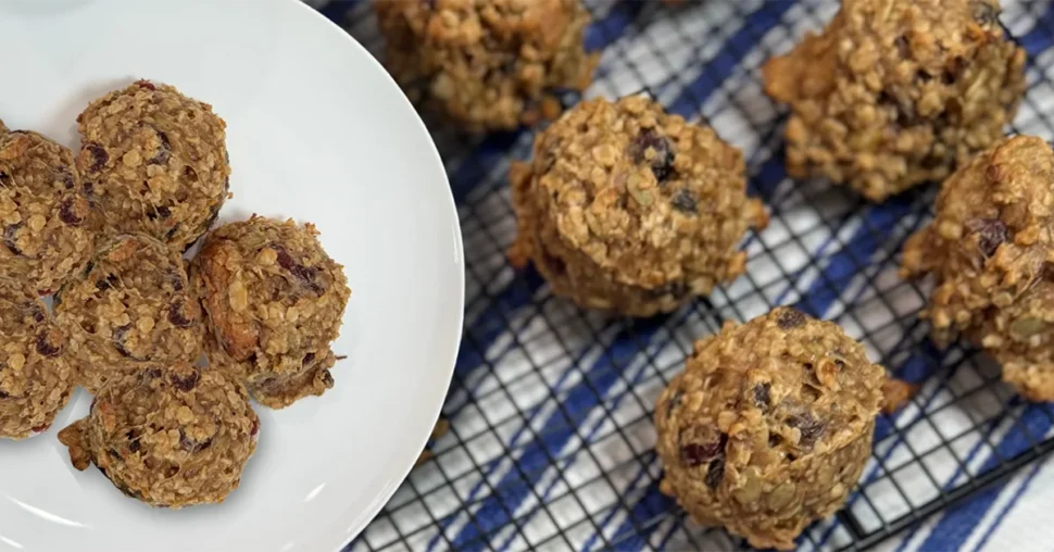 A white plate with six oatmeal cookies sits on a blue checkered cloth next to more cookies on a cooling rack, conveying warmth and homemade appeal.