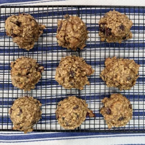 Twelve oatmeal cookies with raisins and nuts are cooling on a black wire rack. The rack rests on a blue and white striped cloth, creating a cozy feel.