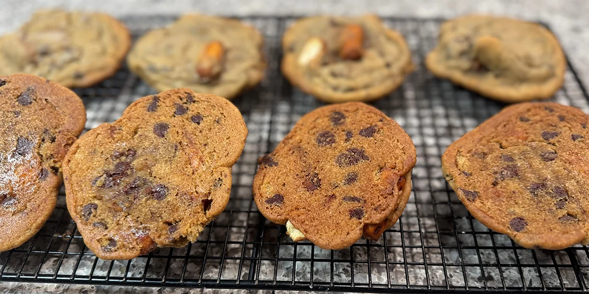 Close-up of homemade, slightly overbaked chocolate chip cookies cooling on a wire rack. The cookies are golden brown with visible chocolate chips.